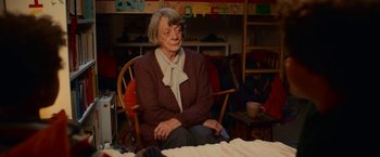 Movie still from “A Boy Called Christmas” (2021), directed by Gil Kenan – An older woman sitting in a chair in a room; Medium shot, Over the shoulder angle