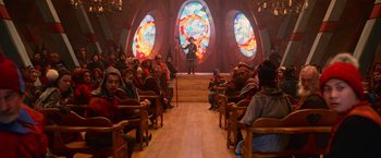Movie still from “A Boy Called Christmas” (2021), directed by Gil Kenan – A group of people sitting in front of a stained glass window; Wide shot, Over the shoulder angle