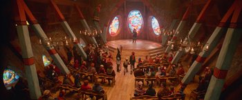 Movie still from “A Boy Called Christmas” (2021), directed by Gil Kenan – A group of people sitting in a room with stained - glass windows; Extreme Wide shot, High angle