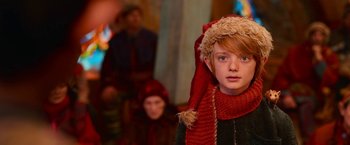 Movie still from “A Boy Called Christmas” (2021), directed by Gil Kenan – A young boy dressed as a christmas elf in front of other people; Close Up shot, Over the shoulder angle