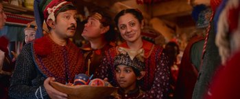 Movie still from “A Boy Called Christmas” (2021), directed by Gil Kenan – A group of people sitting around a table with food on top of it; Medium shot, Over the shoulder angle