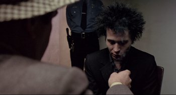 Movie still from “Sid and Nancy” (1986), directed by Alex Cox – A man in a black suit and a black tie; Close Up shot, Over the shoulder angle