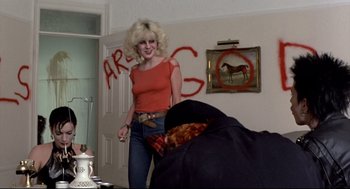 Movie still from “Sid and Nancy” (1986), directed by Alex Cox – A woman standing in front of a wall with graffiti on it; Medium shot, Over the shoulder angle