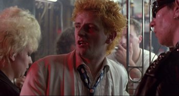 Movie still from “Sid and Nancy” (1986), directed by Alex Cox – A man with blonde curly hair and a white shirt; Close Up shot, Low angle