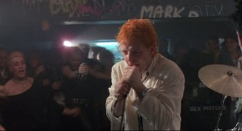 Movie still from “Sid and Nancy” (1986), directed by Alex Cox – A man with red hair singing into a microphone; Medium shot, Low angle