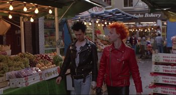 Movie still from “Sid and Nancy” (1986), directed by Alex Cox – A couple of people walking down a street; Medium shot, Over the shoulder angle