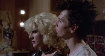 Movie still from “Sid and Nancy” (1986), directed by Alex Cox – A man and a woman are standing next to each other; Close Up shot, Low angle