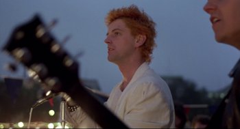 Movie still from “Sid and Nancy” (1986), directed by Alex Cox – A man with red hair is holding a guitar; Close Up shot, Low angle