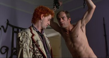 Movie still from “Sid and Nancy” (1986), directed by Alex Cox – A man holding onto a chain while another man watches; Medium shot, Low angle