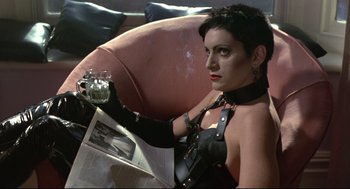 Movie still from “Sid and Nancy” (1986), directed by Alex Cox – A woman sitting in a chair holding a glass of wine; Medium shot, High angle