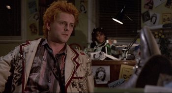 Movie still from “Sid and Nancy” (1986), directed by Alex Cox – A man with a red wig and a jacket on in front of a woman; Medium shot, Over the shoulder angle