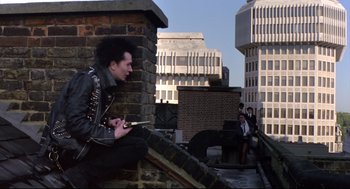 Movie still from “Sid and Nancy” (1986), directed by Alex Cox – A man sitting on top of a brick wall; Wide shot, Low angle