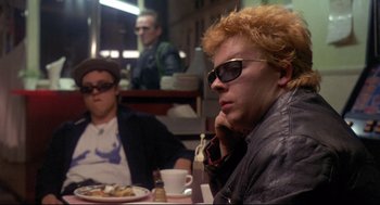 Movie still from “Sid and Nancy” (1986), directed by Alex Cox – A man sitting in front of a plate of food; Medium shot, Over the shoulder angle