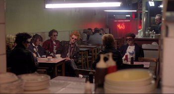 Movie still from “Sid and Nancy” (1986), directed by Alex Cox – A group of people sitting at a table in a restaurant; Wide shot, Over the shoulder angle