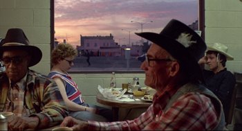 Movie still from “Sid and Nancy” (1986), directed by Alex Cox – An older man sitting at a table with a young boy; Medium shot, Over the shoulder angle