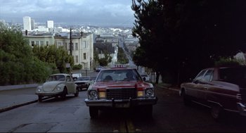 Movie still from “Sid and Nancy” (1986), directed by Alex Cox – An old car is driving down the street in the rain; Extreme Wide shot, Low angle