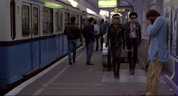 Movie still from “Sid and Nancy” (1986), directed by Alex Cox – A group of people standing on a train platform; Wide shot, High angle