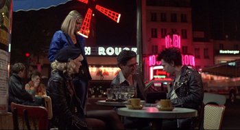 Movie still from “Sid and Nancy” (1986), directed by Alex Cox – A group of people sitting at a table in front of neon lights; Wide shot, Over the shoulder angle