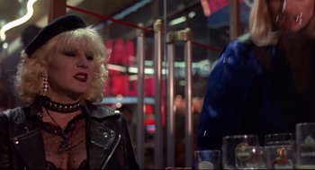 Movie still from “Sid and Nancy” (1986), directed by Alex Cox – A woman in a leather jacket sitting at a table; Close Up shot, Over the shoulder angle