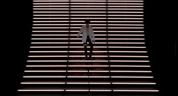 Movie still from “Sid and Nancy” (1986), directed by Alex Cox – A man in a white jacket is walking up some stairs; Extreme Wide shot, Overhead angle