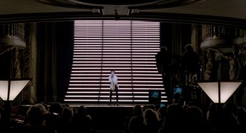 Movie still from “Sid and Nancy” (1986), directed by Alex Cox – A man standing on a stage in front of an audience; Extreme Wide shot, Low angle
