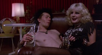 Movie still from “Sid and Nancy” (1986), directed by Alex Cox – A man and a woman sitting next to each other on a couch; Medium shot, Low angle