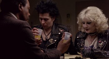 Movie still from “Sid and Nancy” (1986), directed by Alex Cox – A group of people drinking beer at a party; Medium shot, Over the shoulder angle