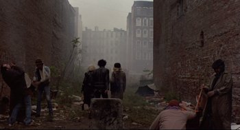 Movie still from “Sid and Nancy” (1986), directed by Alex Cox – Two people are walking through the ruins of an old city; Wide shot, High angle