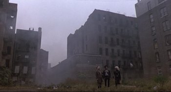 Movie still from “Sid and Nancy” (1986), directed by Alex Cox – A group of people standing on top of a grass covered field; Extreme Wide shot, Low angle