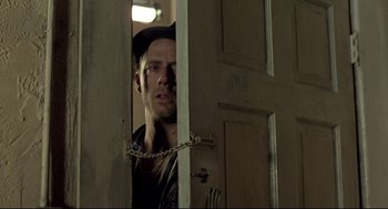Movie still from “Sid and Nancy” (1986), directed by Alex Cox – A man with a chain around his neck looking through a door; Close Up shot, Low angle