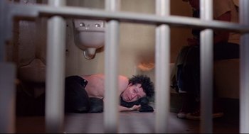 Movie still from “Sid and Nancy” (1986), directed by Alex Cox – A man laying on the ground next to a bathroom sink; Medium shot, Overhead angle