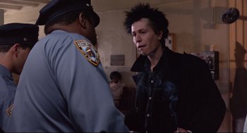Movie still from “Sid and Nancy” (1986), directed by Alex Cox – A police officer talking to a man in a black shirt; Medium shot, Over the shoulder angle