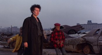 Movie still from “Sid and Nancy” (1986), directed by Alex Cox – Two men standing next to each other near a pile of junk; Medium shot, Low angle