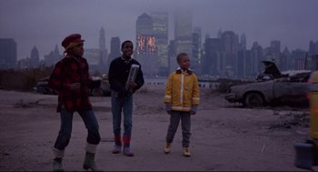 Movie still from “Sid and Nancy” (1986), directed by Alex Cox – A group of kids standing in the sand in front of a city skyline; Wide shot, Low angle