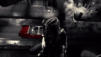 Movie still from “Side by Side” (2012), directed by Christopher Kenneally – A woman in black jacket standing next to a red car on a street; Wide shot, Overhead angle
