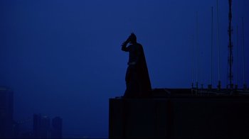 Movie still from “Side by Side” (2012), directed by Christopher Kenneally – A statue of a batman in the dark with a city in the background; Wide shot, Low angle