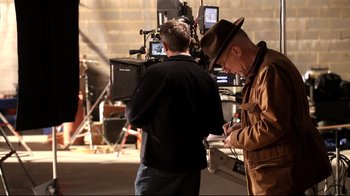 Movie still from “Side by Side” (2012), directed by Christopher Kenneally – Two men are standing next to each other in front of a video camera; Medium shot, Over the shoulder angle