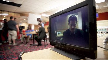 Movie still from “Side by Side” (2012), directed by Christopher Kenneally – A television screen with a man on it in a room with people around it; Medium shot, Over the shoulder angle