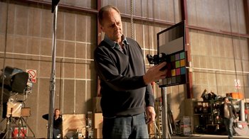 Movie still from “Side by Side” (2012), directed by Christopher Kenneally – A man holding a color chart in front of a camera; Medium shot, Over the shoulder angle