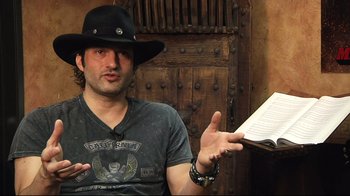 Movie still from “Side by Side” (2012), directed by Christopher Kenneally – A man wearing a black hat and holding a book; Close Up shot, High angle