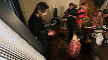 Movie still from “Side by Side” (2012), directed by Christopher Kenneally – A group of people standing around a room; Medium shot, Over the shoulder angle