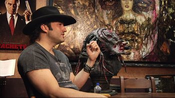 Movie still from “Side by Side” (2012), directed by Christopher Kenneally – A man sitting at a table with a mask on his head; Medium shot, Over the shoulder angle