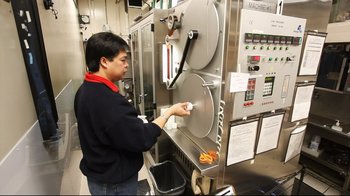 Movie still from “Side by Side” (2012), directed by Christopher Kenneally – A man in black jacket putting food into a machine; Medium shot, Low angle