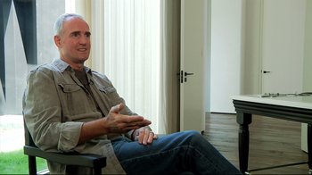 Movie still from “Side by Side” (2012), directed by Christopher Kenneally – A man sitting on a chair in a room; Medium shot, Over the shoulder angle