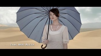 Movie still from “Side by Side” (2012), directed by Christopher Kenneally – A woman holding an umbrella while standing on a beach; Medium shot, Low angle