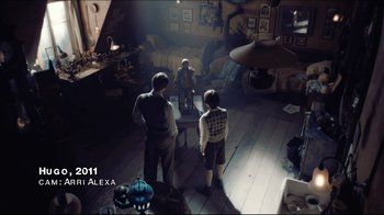 Movie still from “Side by Side” (2012), directed by Christopher Kenneally – Two men and a woman standing in a living room; Wide shot, High angle