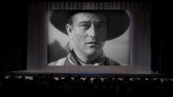 Movie still from “Side by Side” (2012), directed by Christopher Kenneally – A man in a cowboy hat is on a large screen; Wide shot, Low angle