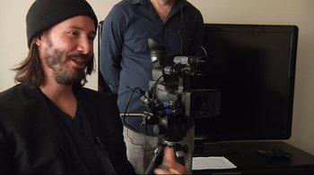 Movie still from “Side by Side” (2012), directed by Christopher Kenneally – A man holding a video camera in front of another man in front of a television; Close Up shot, Over the shoulder angle