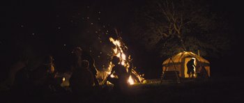Movie still from “Sightseers” (2012), directed by Ben Wheatley – A group of people sitting around a fire at night; Wide shot, Over the shoulder angle