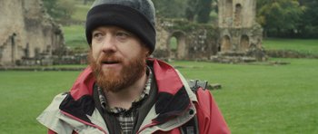 Movie still from “Sightseers” (2012), directed by Ben Wheatley – A man with a beard wearing a red jacket and a black hat; Close Up shot, Over the shoulder angle